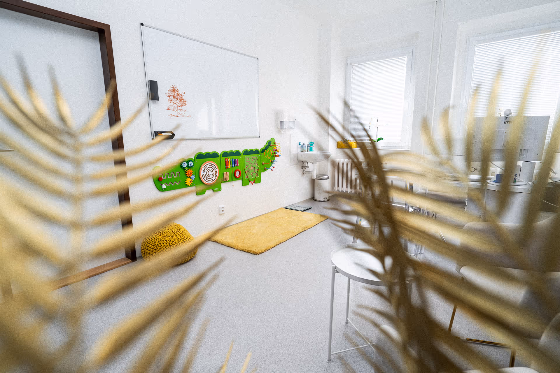 Bright children's playroom with a green crocodile-shaped wall activity board, yellow rug, whiteboard, and sink.
