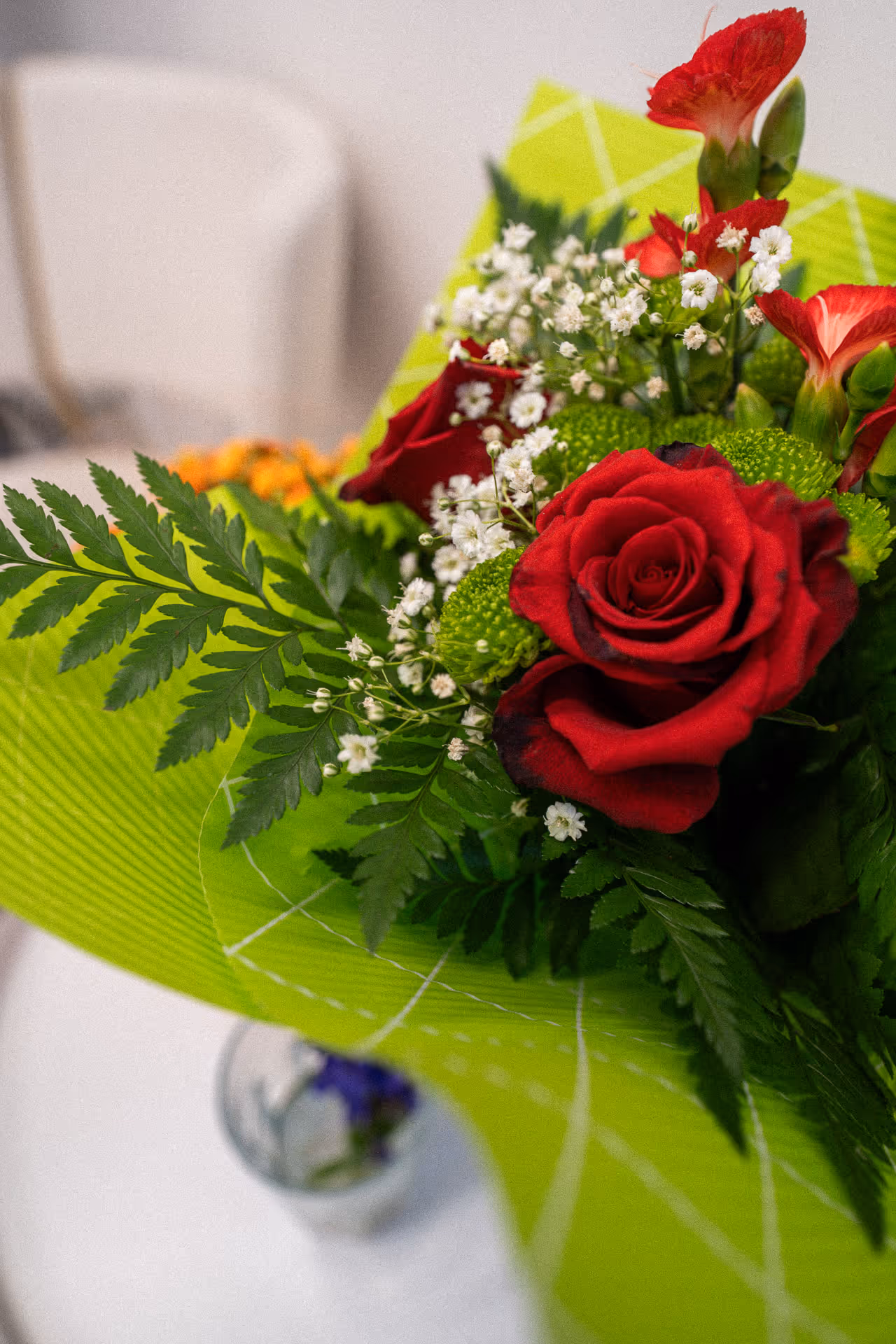 Close-up of a bouquet with red roses, small white flowers, green foliage, and wrapped in bright green paper.