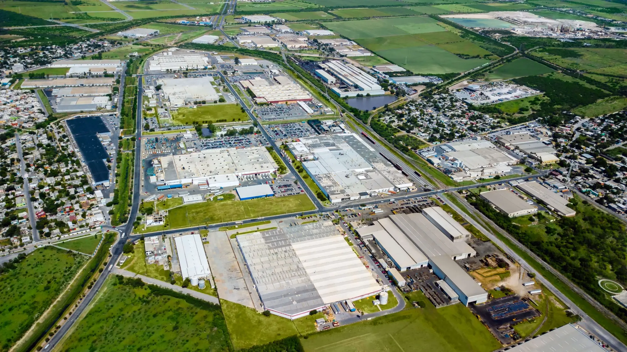 Aerial view of an industrial park with multiple large warehouse buildings, parking lots, roads, and green fields surrounding the area.