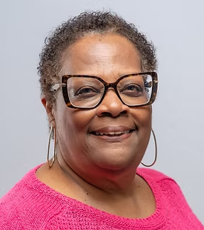 A headshot of a black woman wearing glasses and a pink shirt
