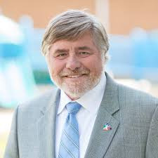 A headshot of a white man wearing a gray suit and blue tie