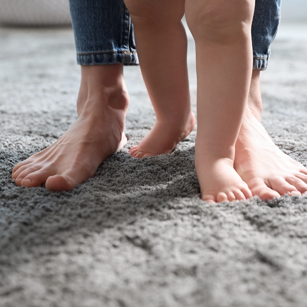 Adult and child barefoot standing together on a soft gray carpet.
