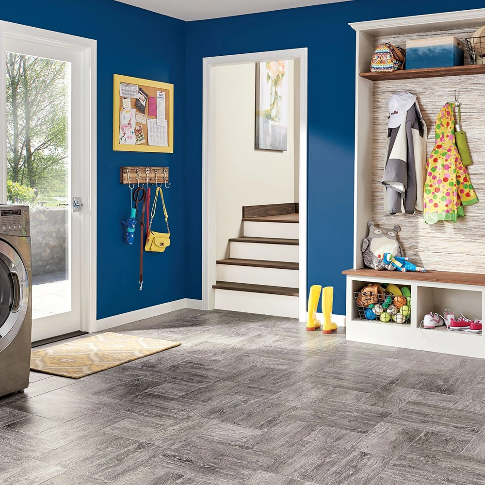 Bright mudroom with blue walls, gray patterned flooring, a washing machine, coat hooks, a staircase, and storage cubbies with shoes and toys.