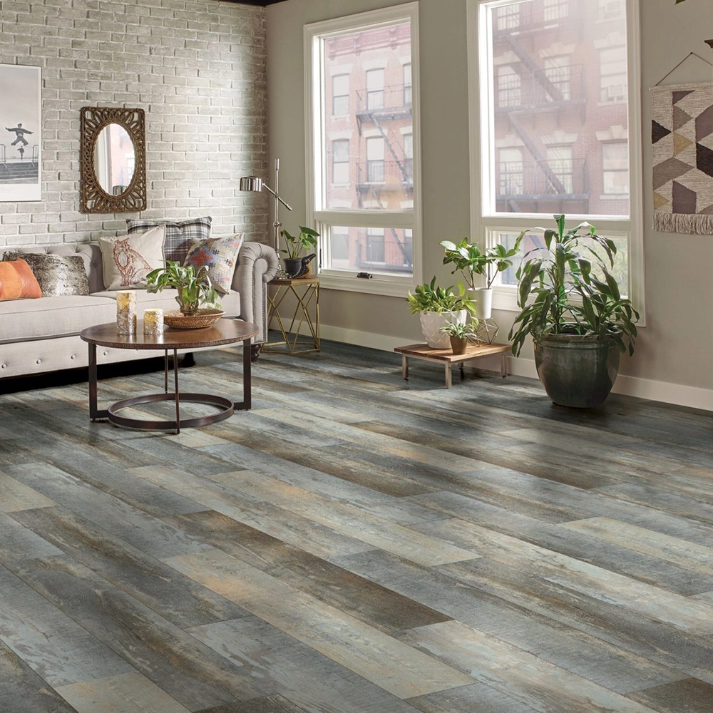 Living room with gray and beige wood plank flooring, beige sofa with colorful pillows, round wooden coffee table, and potted plants by two large windows.