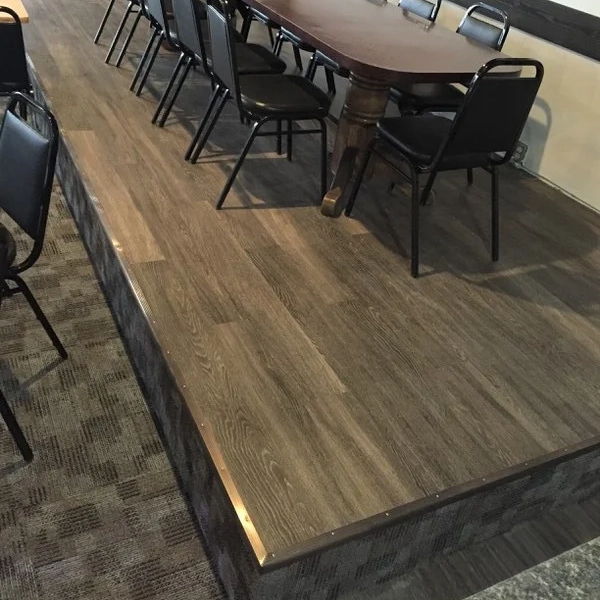 Raised wooden platform with a dark wood table and black chairs arranged around it in a room with carpeted floor.