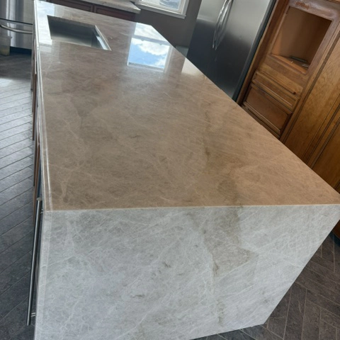 Modern kitchen island with Taj Mahal granite waterfall edge installation, updated backsplash and dark wood cabinetry nearly complete