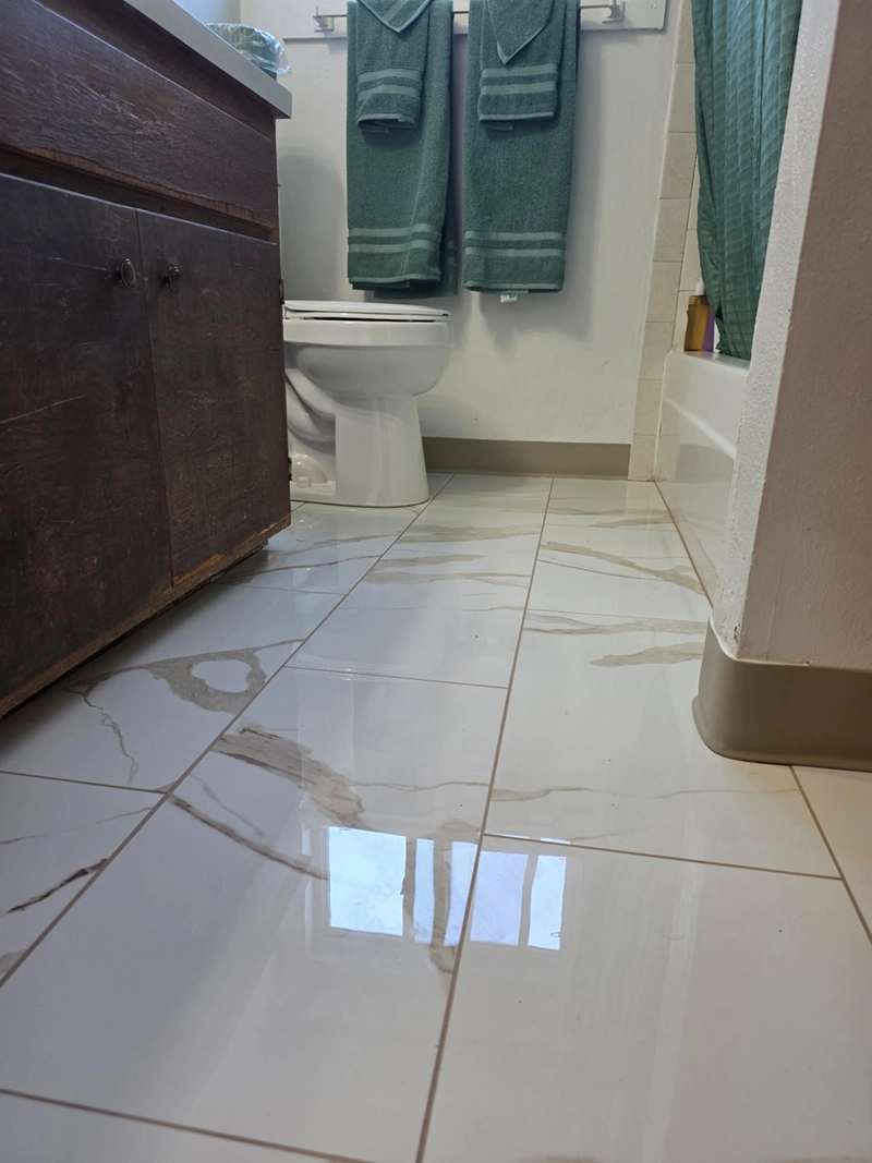 Glossy marble-look porcelain tile with light brown grout covering a small bathroom floor.