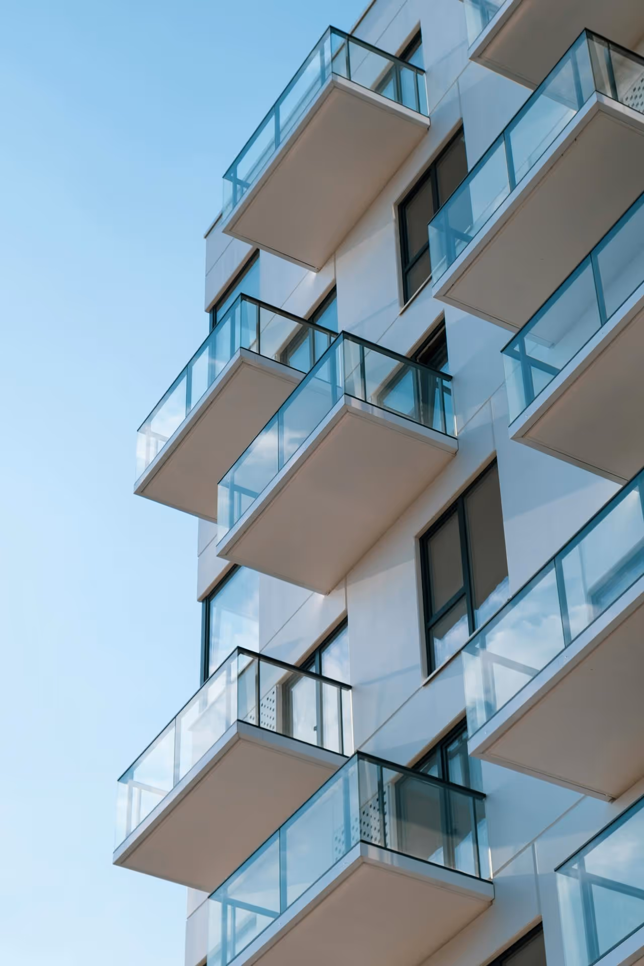 Modern apartment building balconies with glass railings against a clear blue sky.