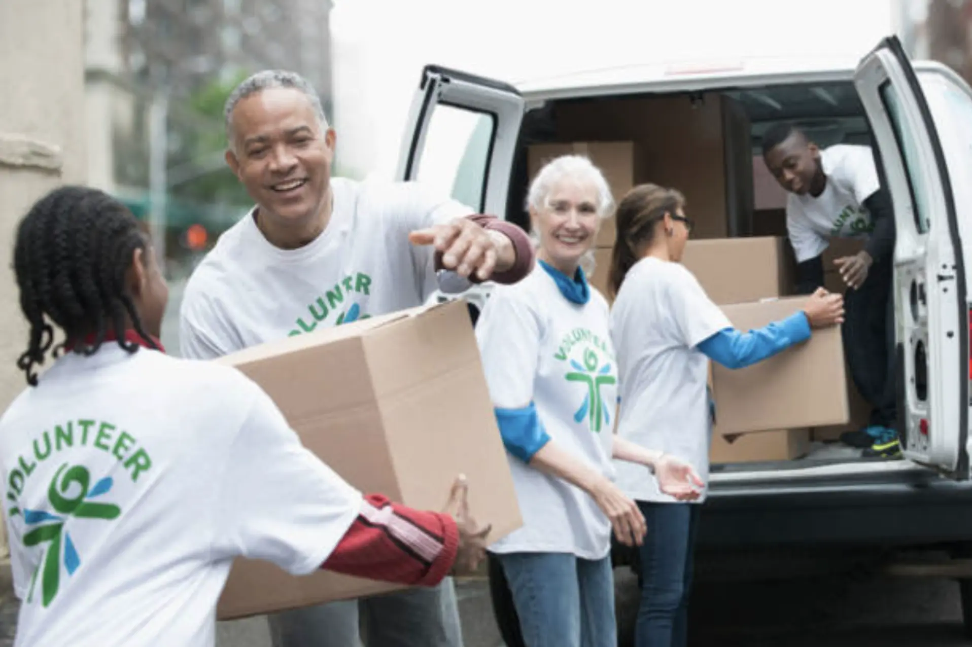 A diverse group of volunteers unloading cardboard boxes from a white van outdoors.