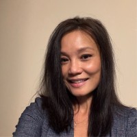 Smiling woman with long dark hair wearing a dark blazer against a plain beige background.