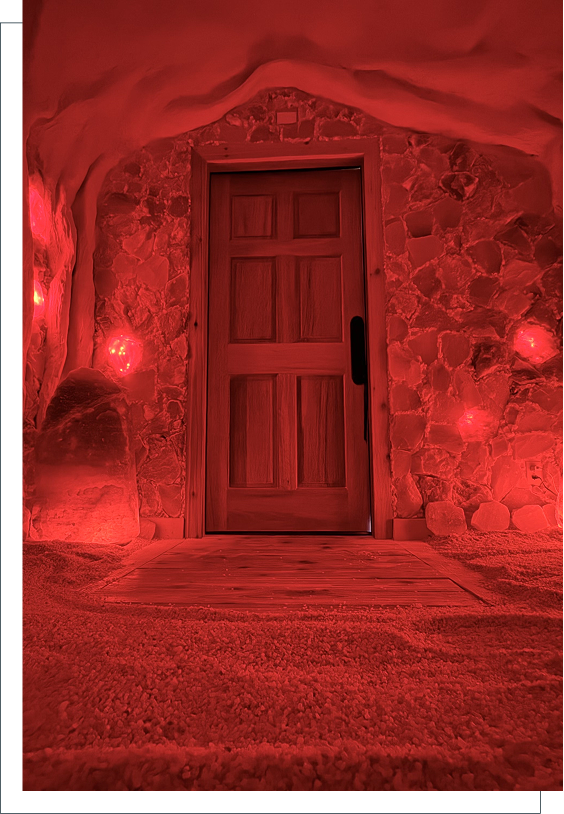 Wooden door set in a stone wall illuminated by red lighting with rocky ground and glowing salt lamps.
