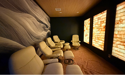 A salt room with illuminated salt wall panels, white crystal singing bowls on the floor, and beige reclining chairs.