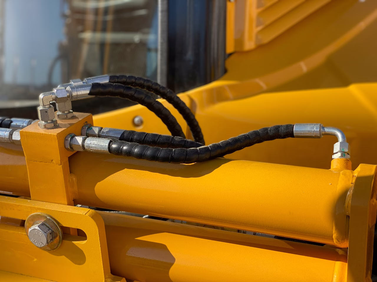 Technician inspecting hydraulic system components on heavy equipment, checking hoses, fittings, and fluid lines during maintenance service outdoors.