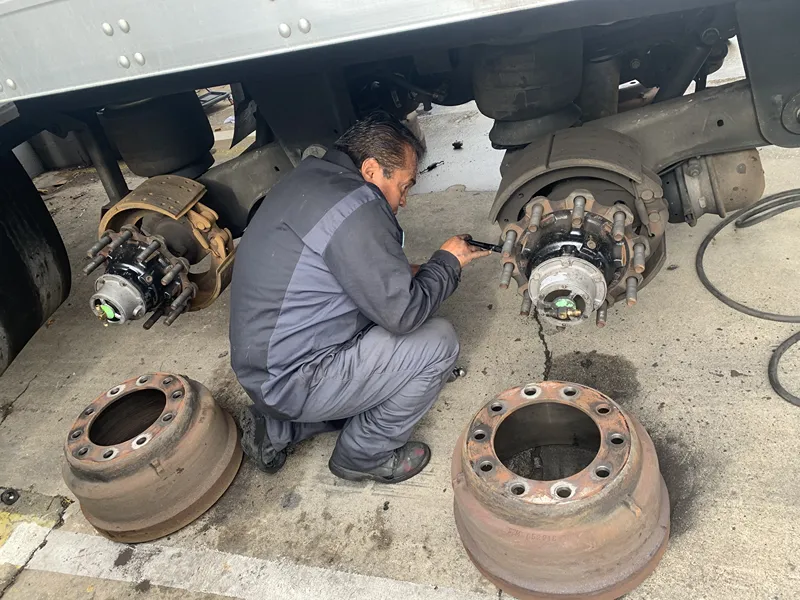 Technician performs heavy-duty brake service on a truck with brake drums removed for inspection.