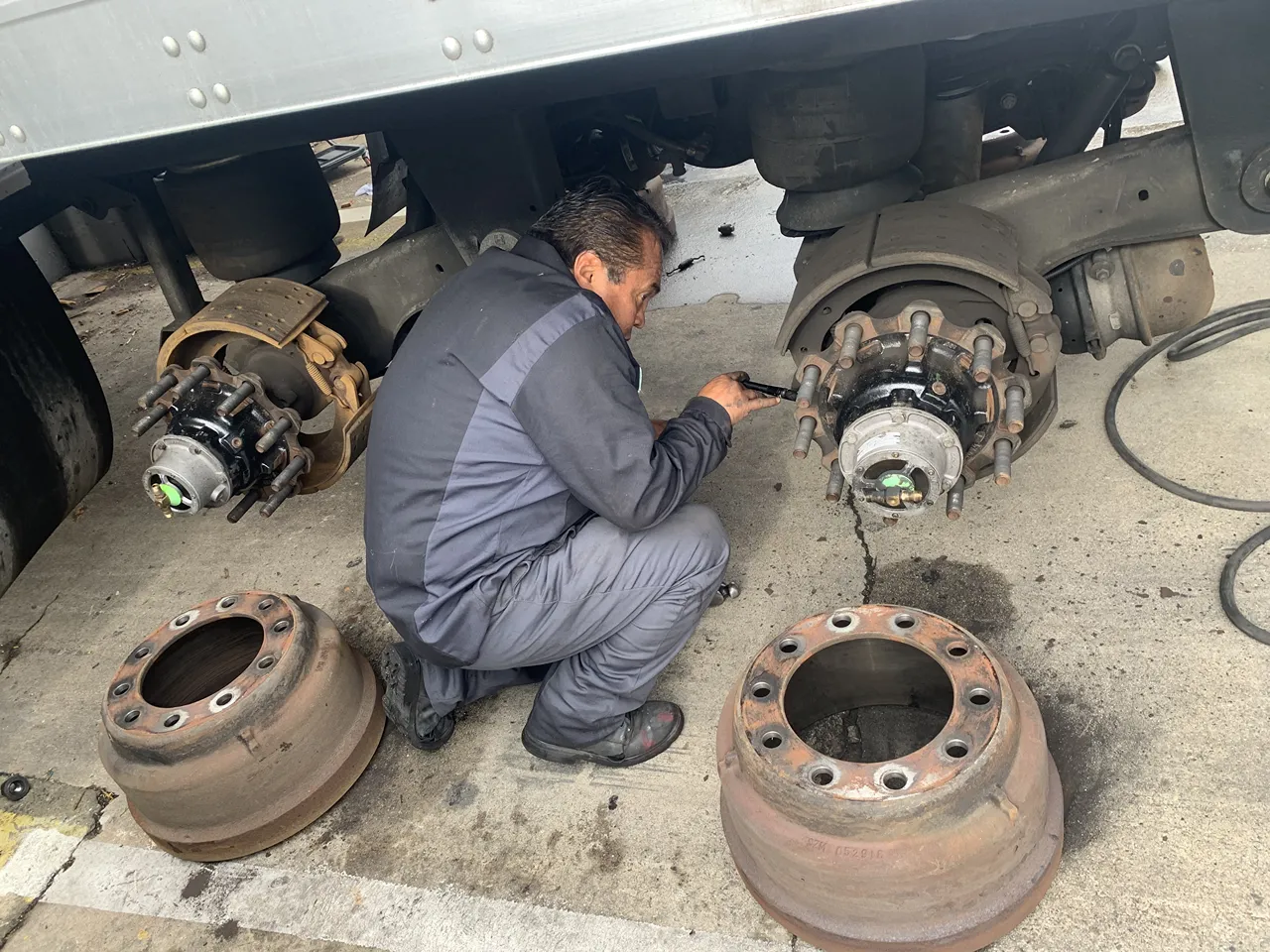 Technician performs heavy-duty brake service on a truck with brake drums removed for inspection.