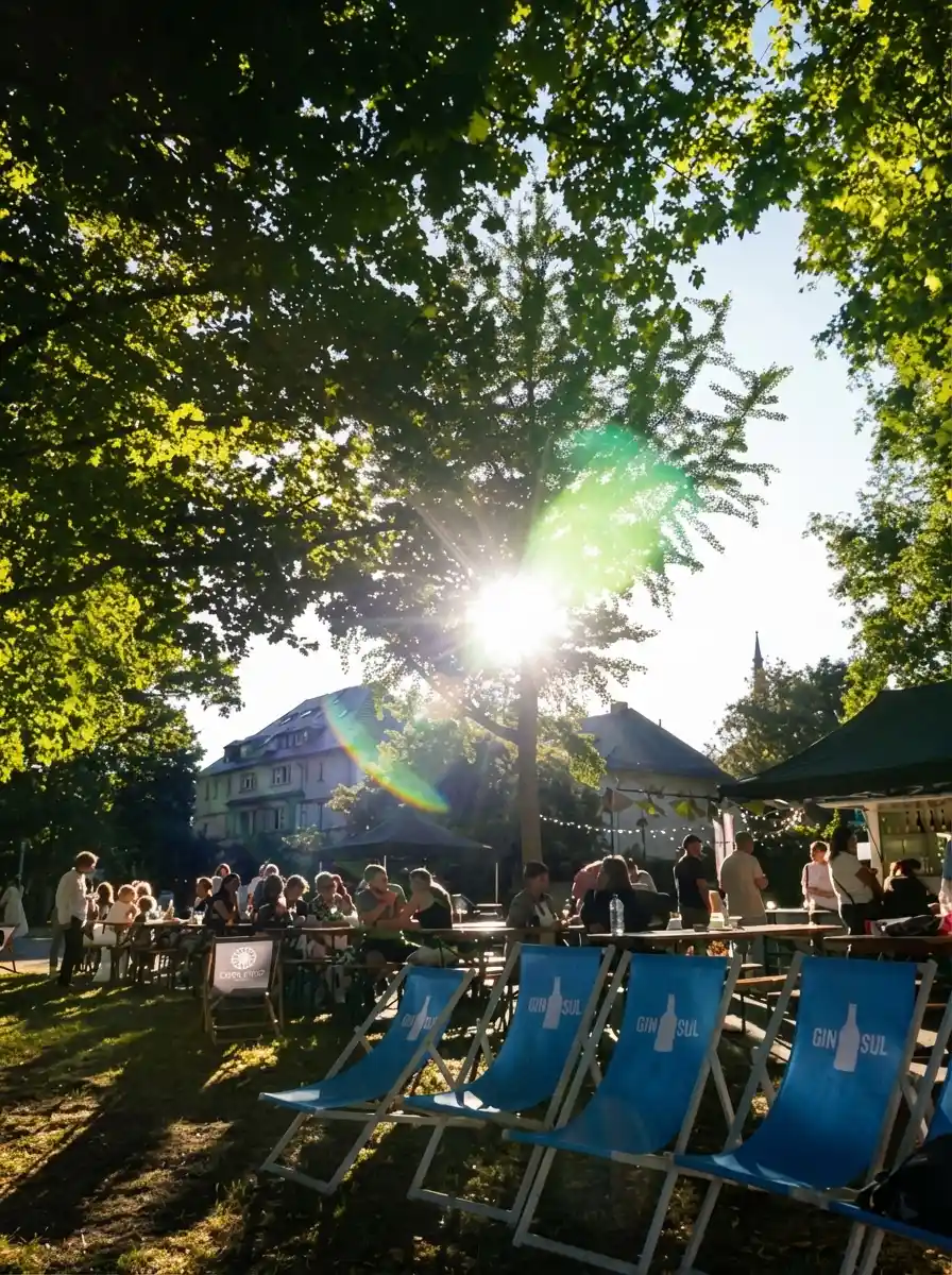 Vorne sind paar Strandliegend und im Hinterrgund sitzen Menschen auf Bierbänke und trinken Wein