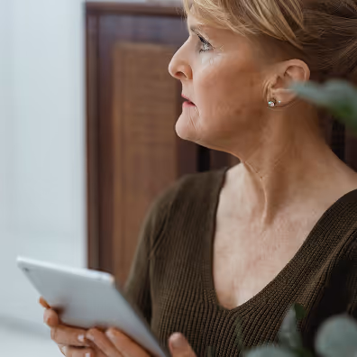 Profile of a middle-aged woman looking to the side while holding a tablet indoors.