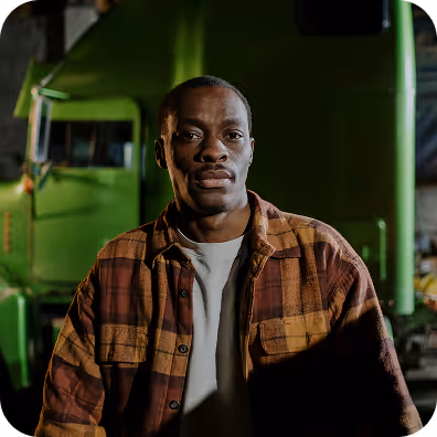 Man wearing a brown plaid shirt standing in front of a green truck at night.