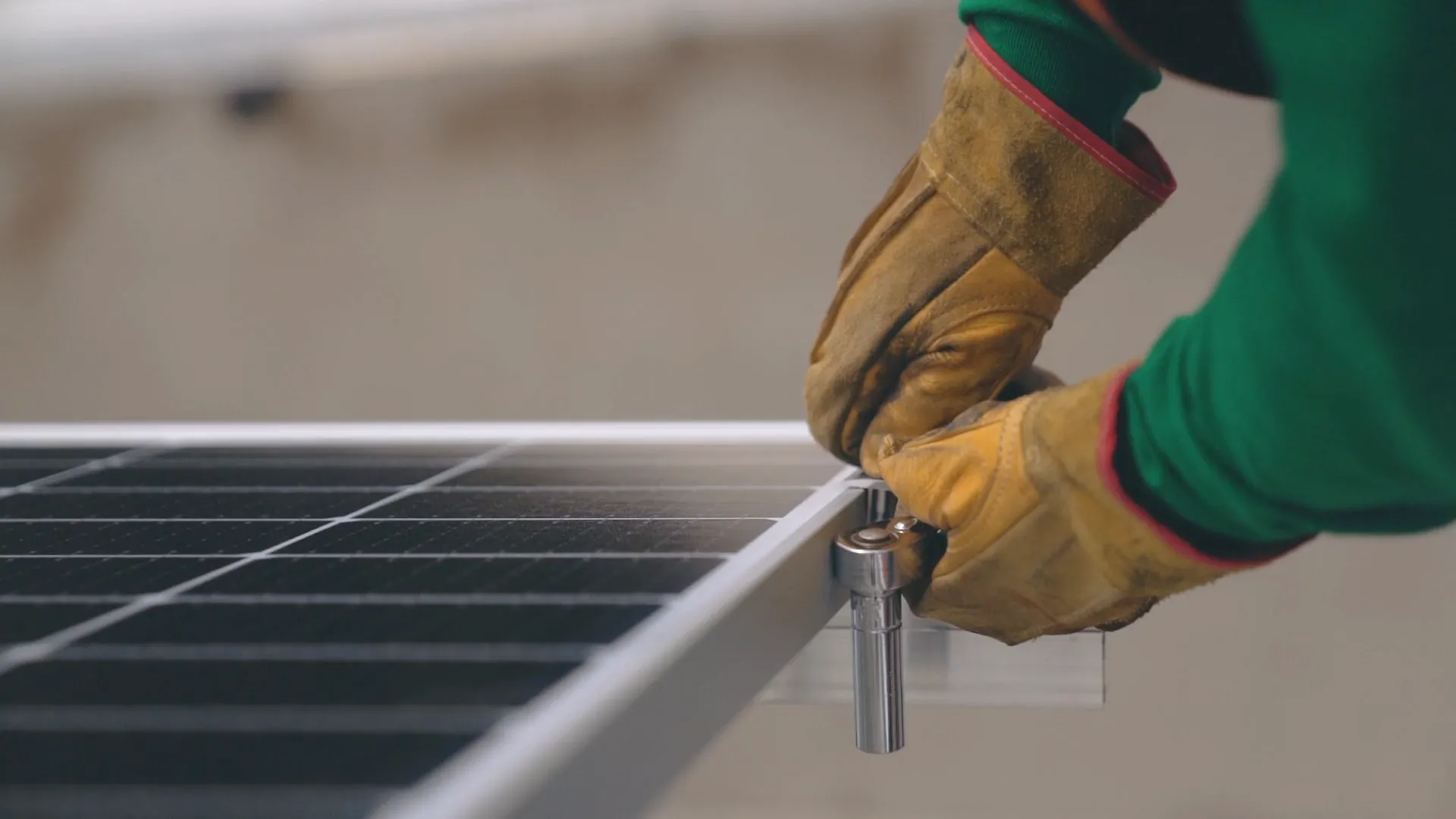 Hands wearing yellow work gloves tightening a bolt on the corner of a solar panel frame with a wrench.