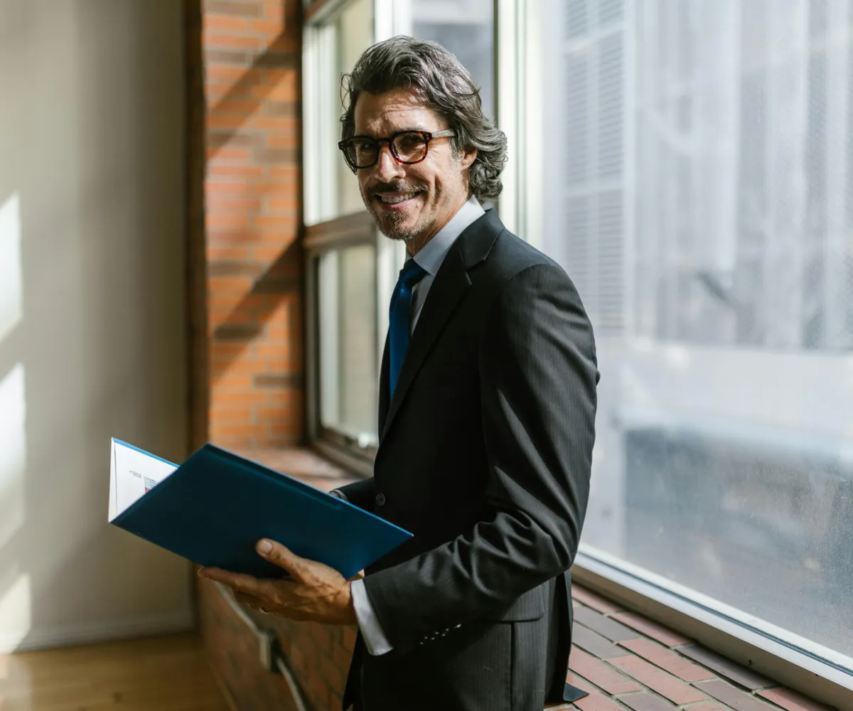 Man wearing a brown and orange plaid shirt standing in front of a green truck in a dimly lit garage.