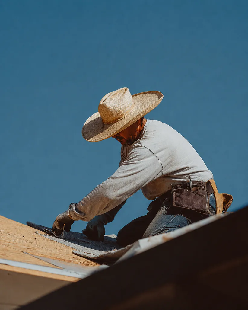 Man wearing a large straw hat working on a rooftop under a clear blue sky.