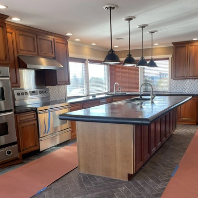 Before the remodel: the original dark concrete island and countertops with wood cabinets and pendant lights.