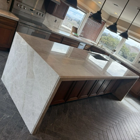 Remodeled kitchen with a Taj Mahal quartzite waterfall island, matching countertops, and pendant lighting.