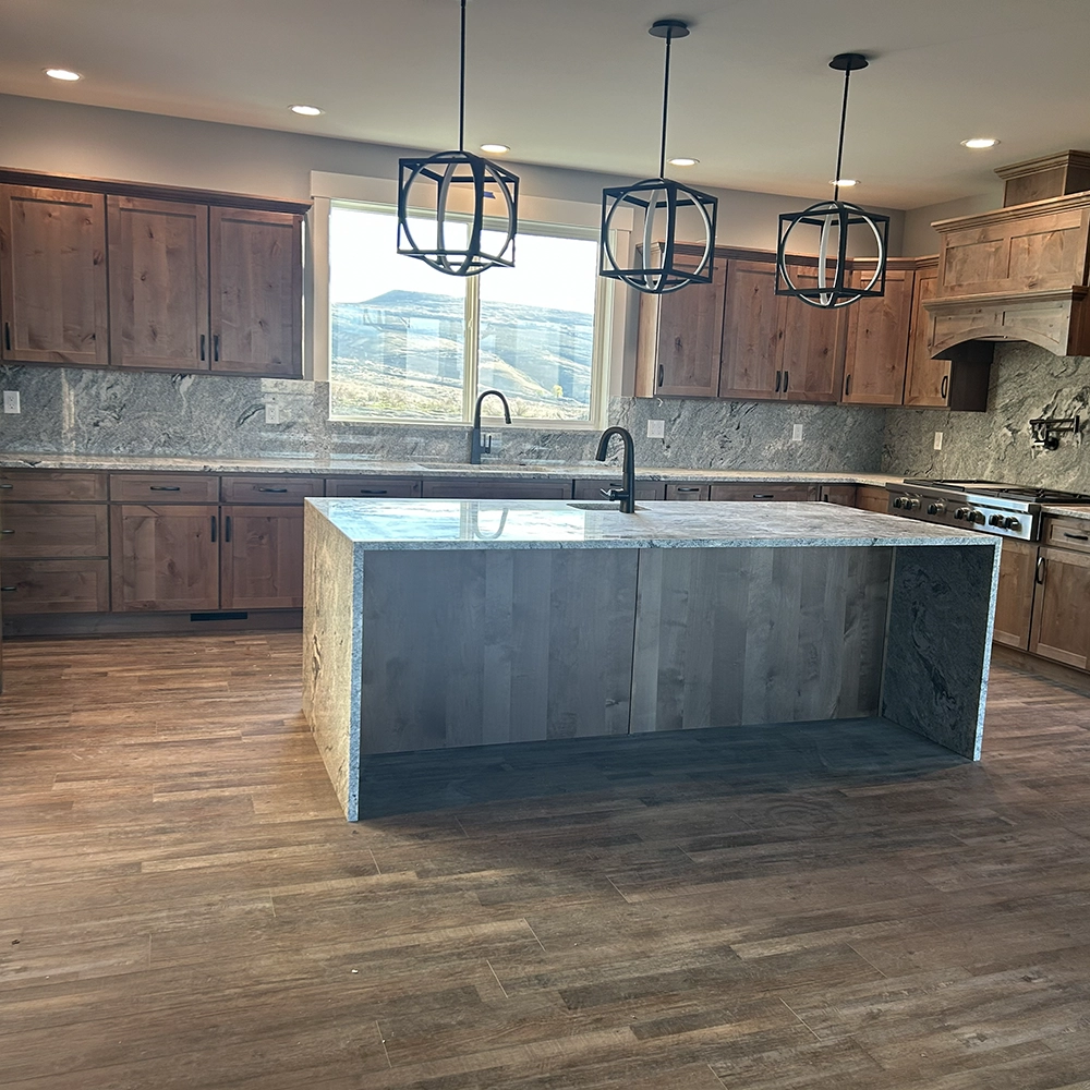Granite countertops and island beneath three pendant lights, with a large window framing a mountain view.