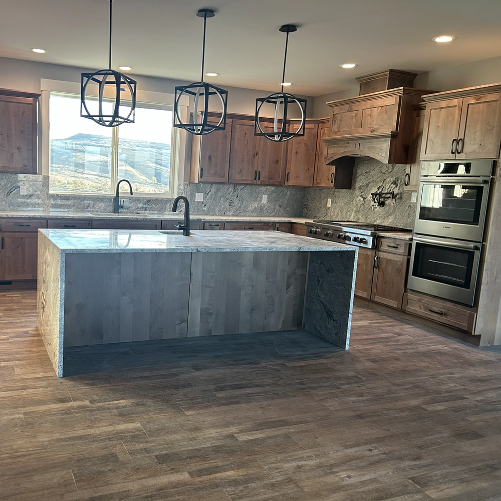 Spacious kitchen with wood cabinets, granite countertops, a large central island, and three pendant lights.