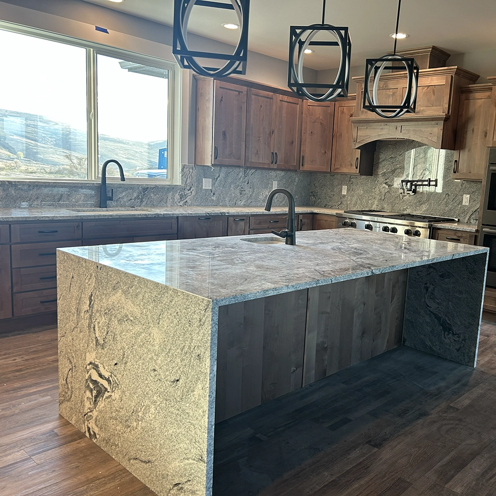 Kitchen with wood cabinets, granite countertops, and a large granite island with a sink under black pendant lights.