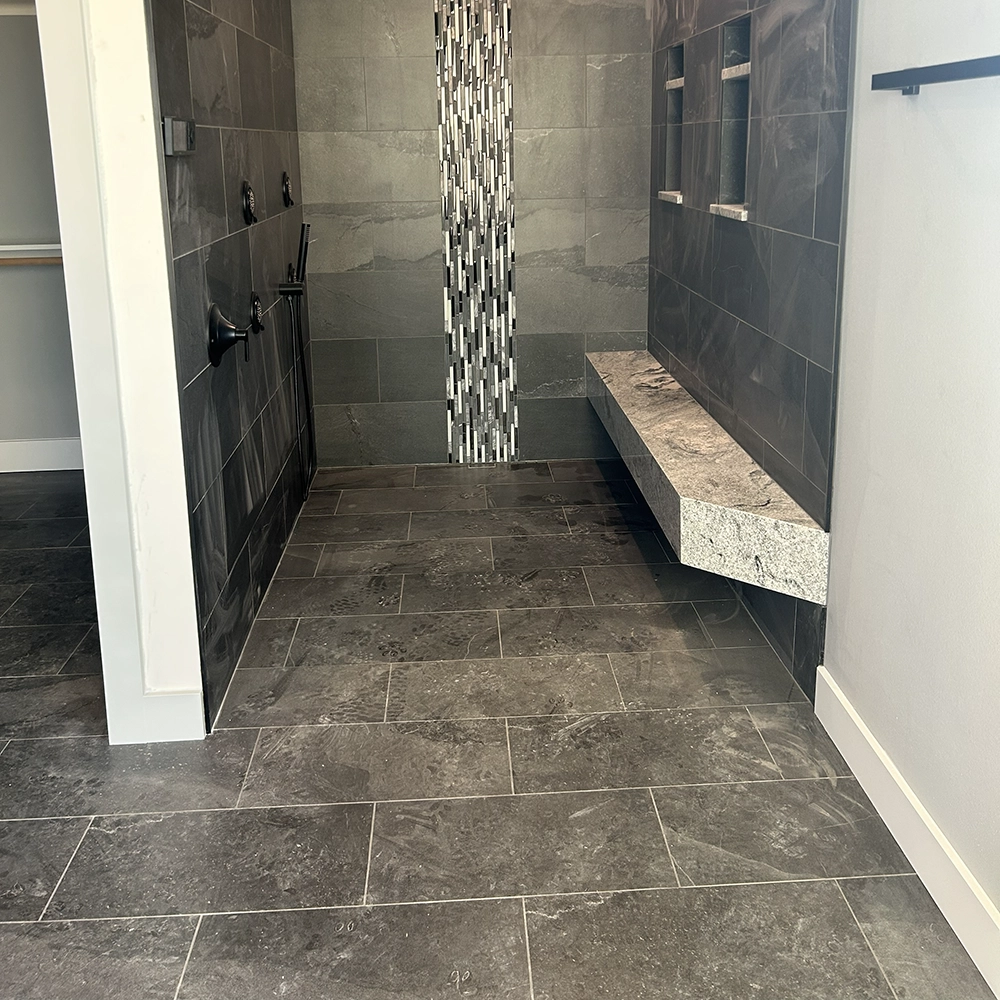 Walk-in shower with dark gray tile, a vertical mosaic accent, a built-in bench, and three shower controls.