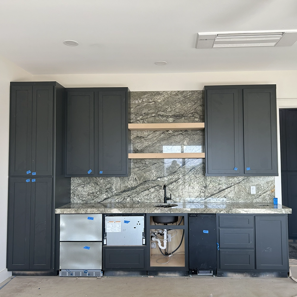 Granite countertop and full-height granite backsplash with floating wood shelves in a rec room kitchen.