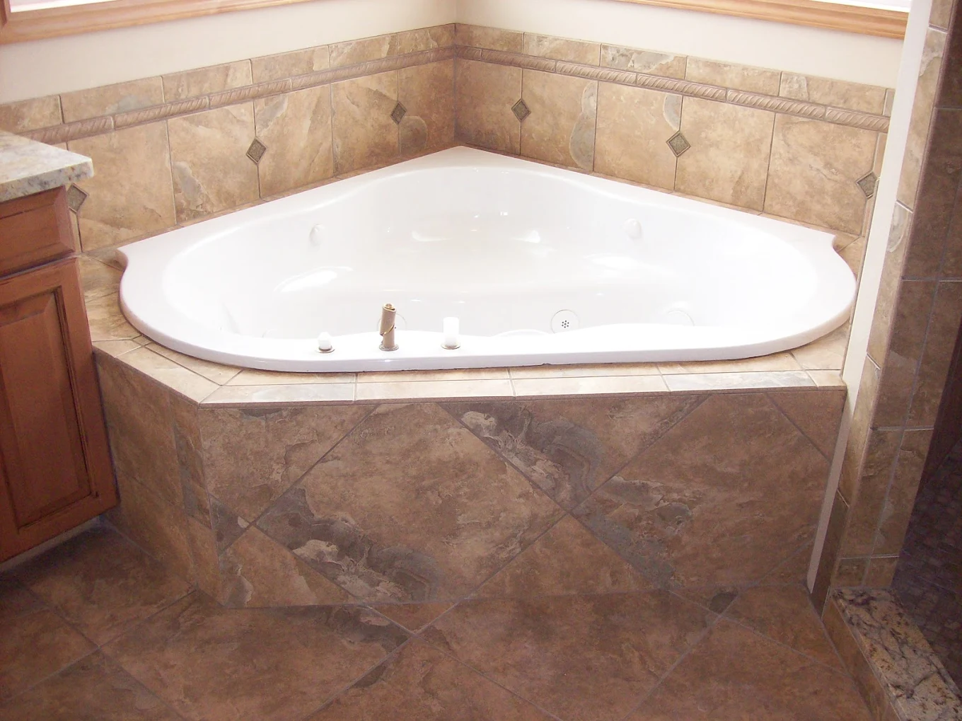 Corner bathtub with a white interior surrounded by a beige and brown tiled platform and walls.