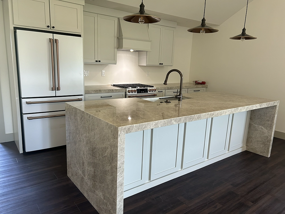 Taj Mahal quartzite island with waterfall edges in a bright kitchen with white cabinets.