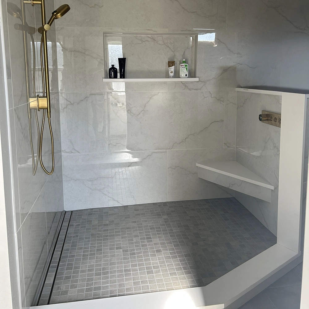 Walk-in shower with 24 by 48 porcelain wall tile and a corner bench capped in quartz.