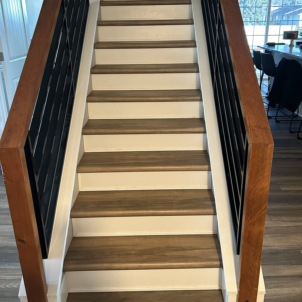Interior staircase with light brown luxury vinyl plank treads, white risers, and black metal railings.