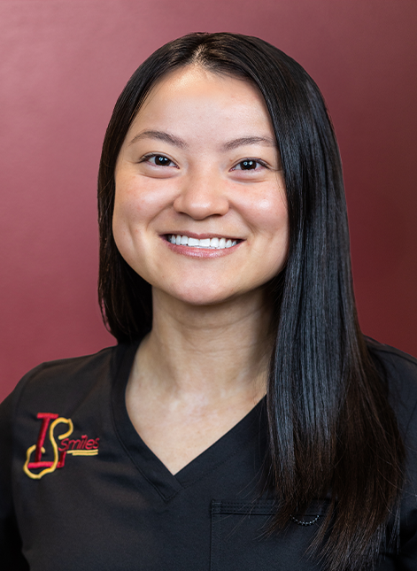 Portrait of Jade smiling in black scrubs against a burgundy background.