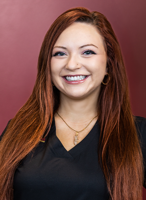 Portrait of Amy smiling in black scrubs against a burgundy background.