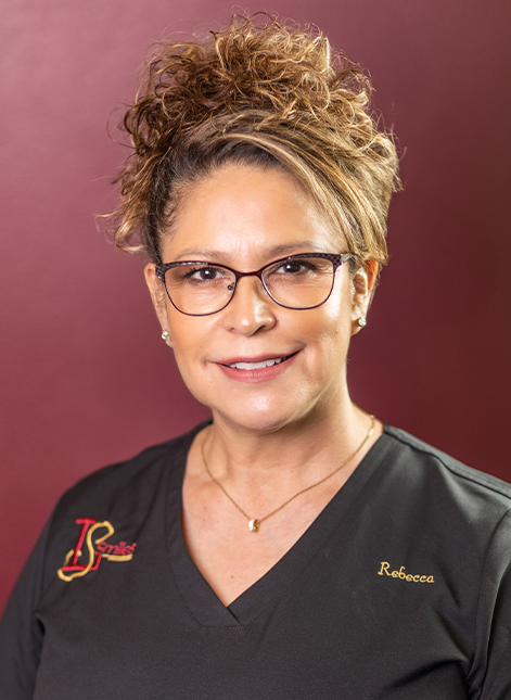 Portrait of Rebecca smiling in black scrubs against a burgundy background.