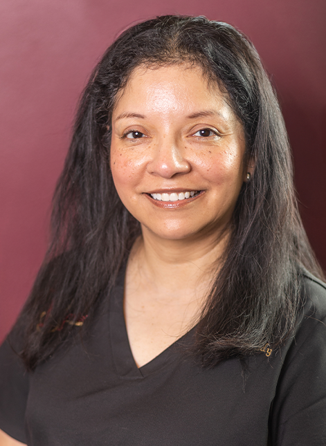 Portrait of Cindy smiling in black scrubs against a burgundy background.