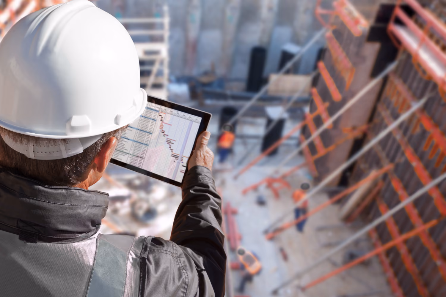 Construction worker in a white helmet reviewing a project timeline on a tablet at a site.
