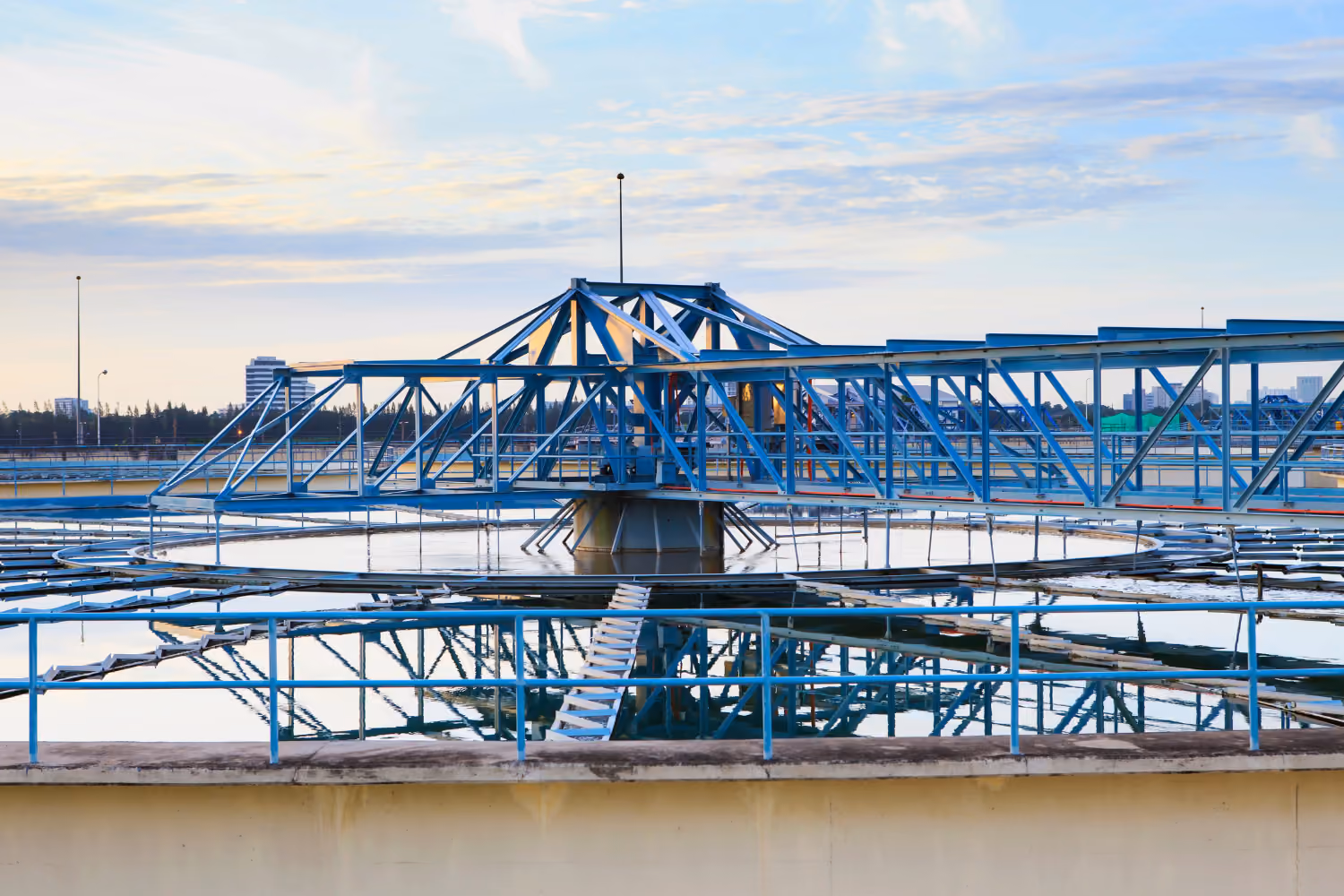 Large circular water treatment facility with blue metal framework and reflections in water.