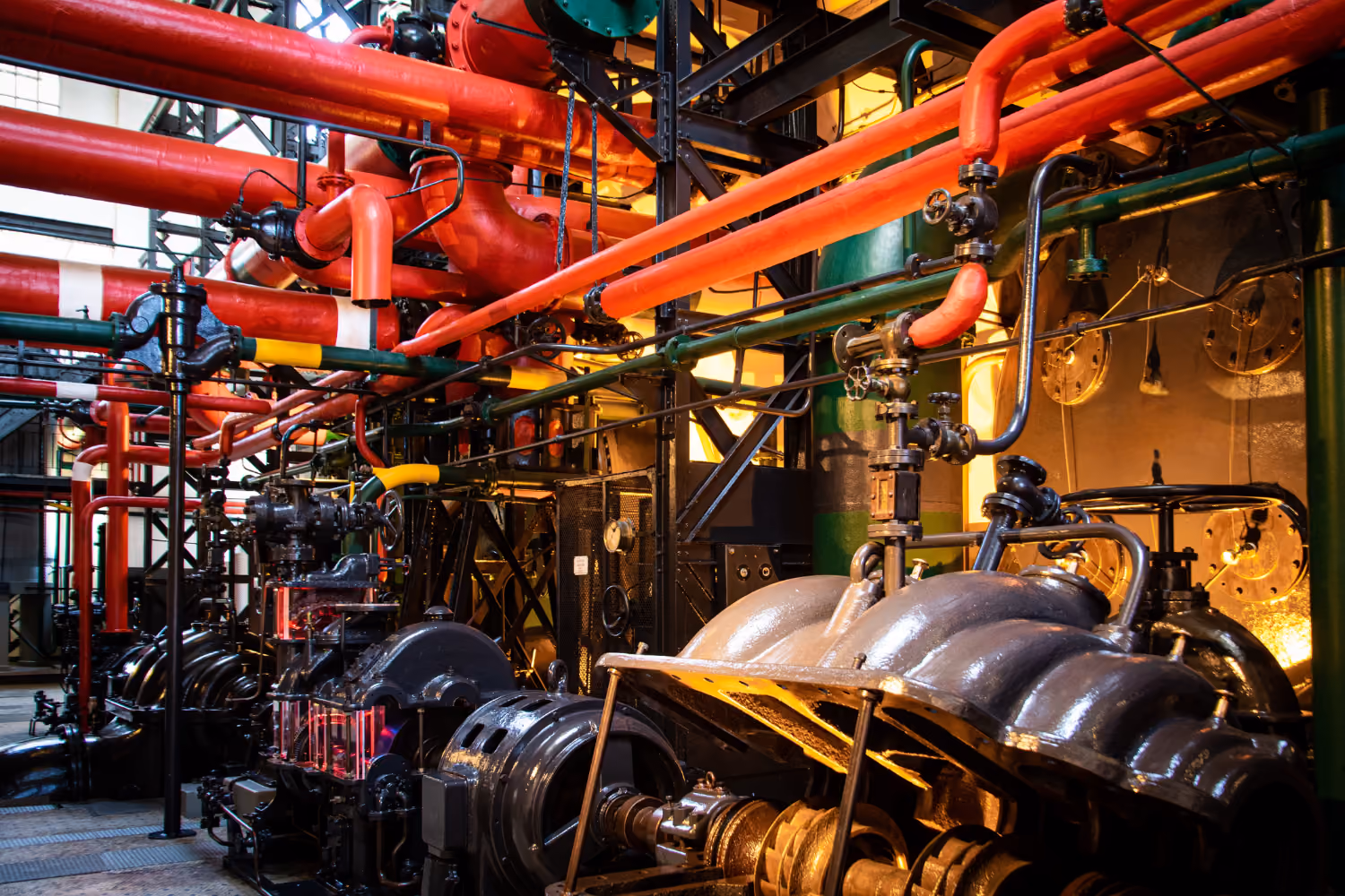 Industrial plant interior featuring large machinery, piping systems and engineering infrastructure.