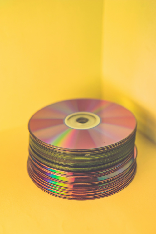stack of compact discs with rainbow reflections on a bright yellow background