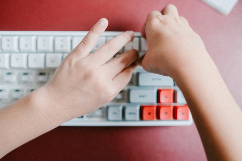 close-up of a child’s hands typing on a computer keyboard with white and red keys