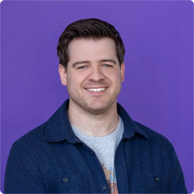 Smiling young man with short brown hair, wearing a dark blue jacket over a gray shirt, against a purple background.