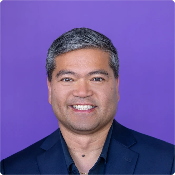 Smiling middle-aged man with salt-and-pepper hair wearing a dark blazer against a purple background.