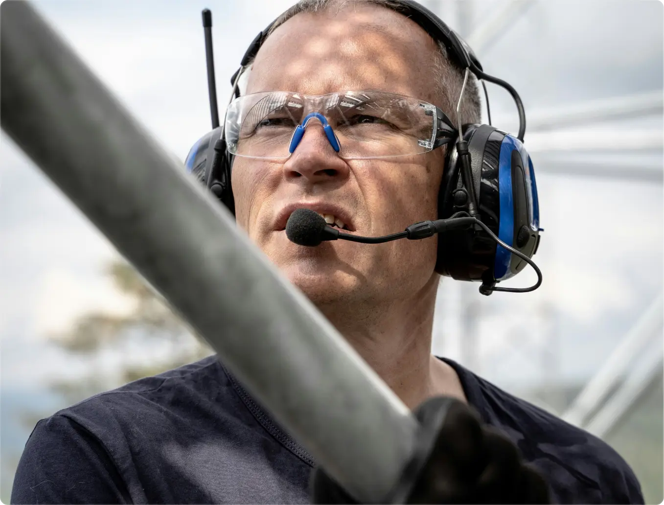 Smiling man wearing glasses holds two young children, one on his shoulders and the other in his arms, outdoors near a white fence.