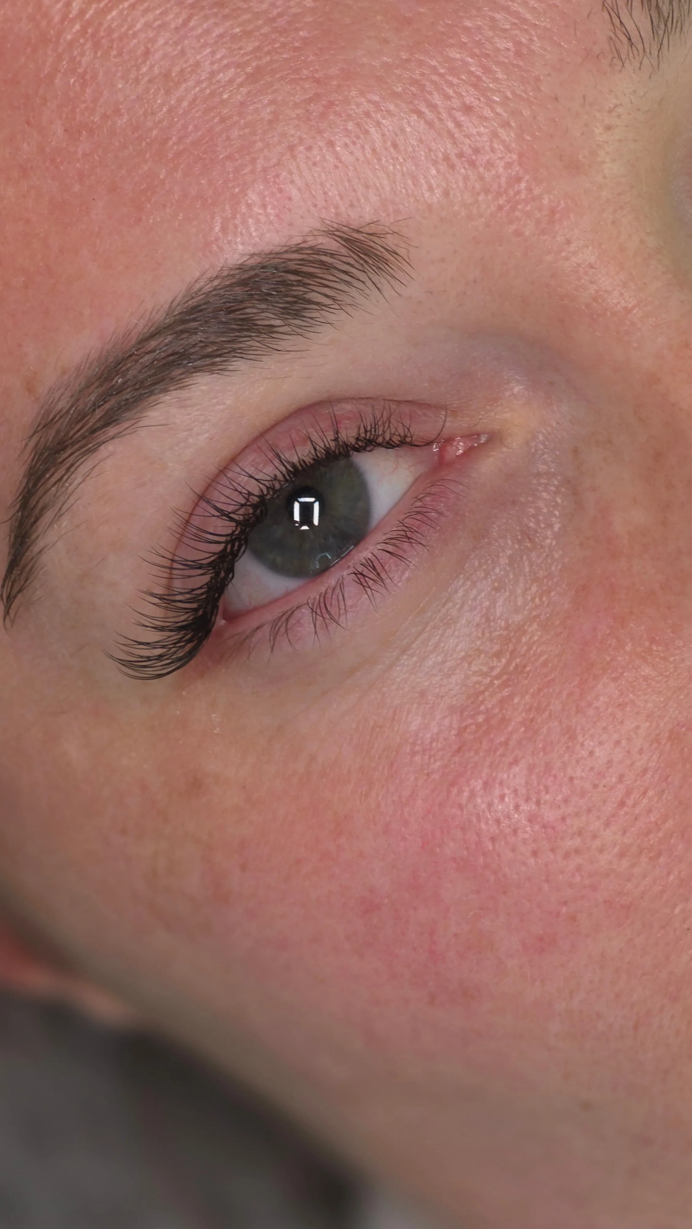 Close-up of a person's eye with long eyelashes and a well-groomed eyebrow on slightly flushed skin.