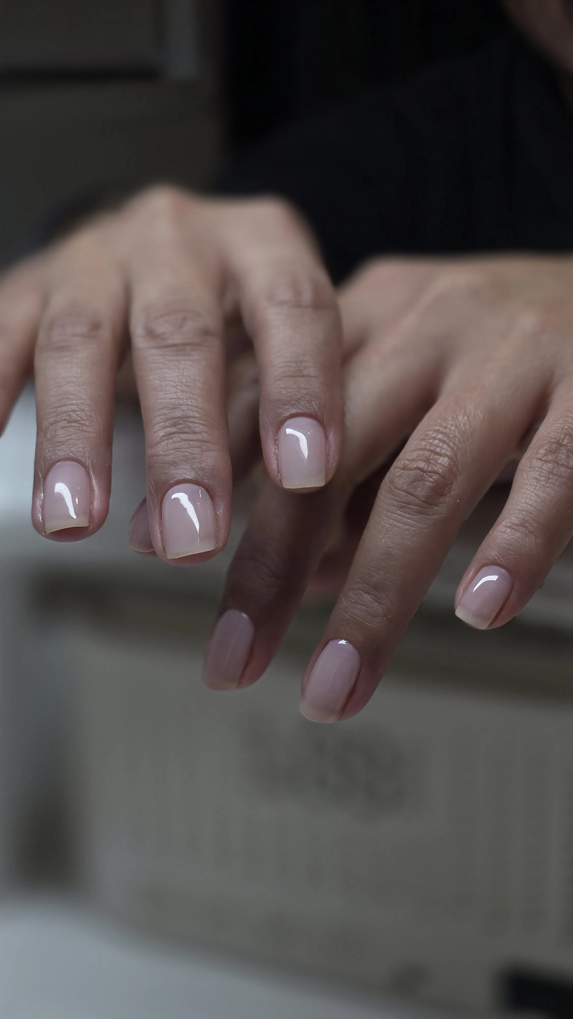 Hands with neatly manicured nails painted in a natural pale pink shade with a glossy finish.